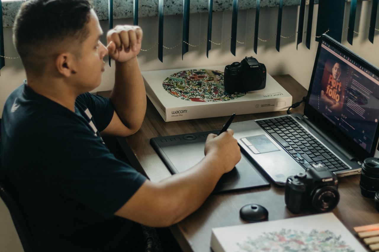 Un photographe travaillant dans un environnement créatif avec un ordinateur portable et une tablette Wacom, concentré sur l’édition de photos en intérieur.